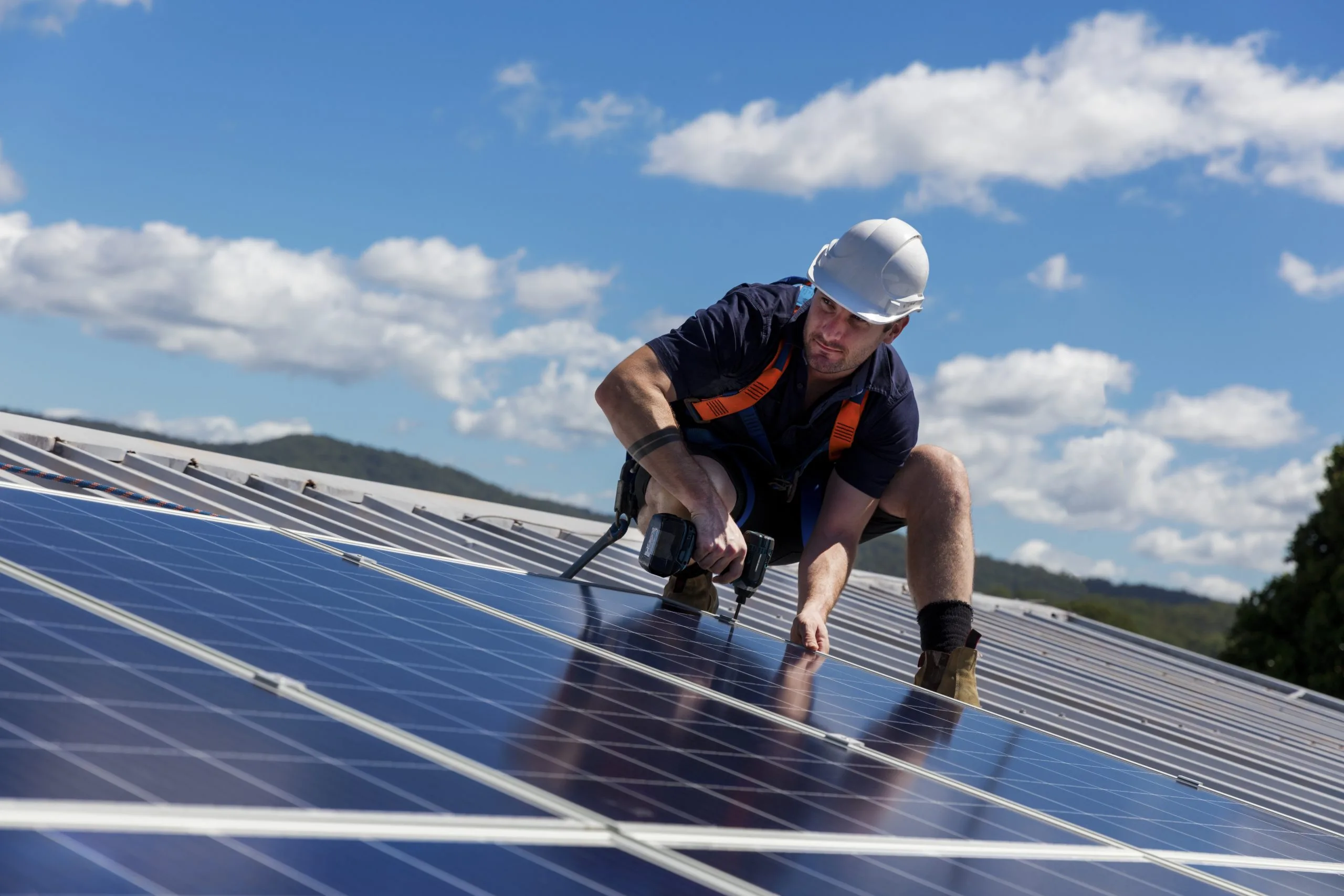 Solar panel installer with drill installing solar panels on roof on a sunny day